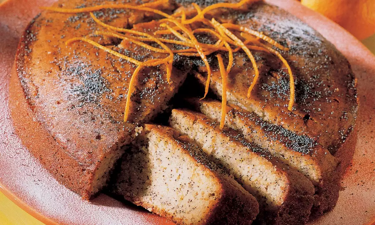 Runder, saftiger Orangen-Mohn-Kuchen mit goldbrauner Kruste und feinen Orangenzesten, angerichtet auf einem hellen Teller