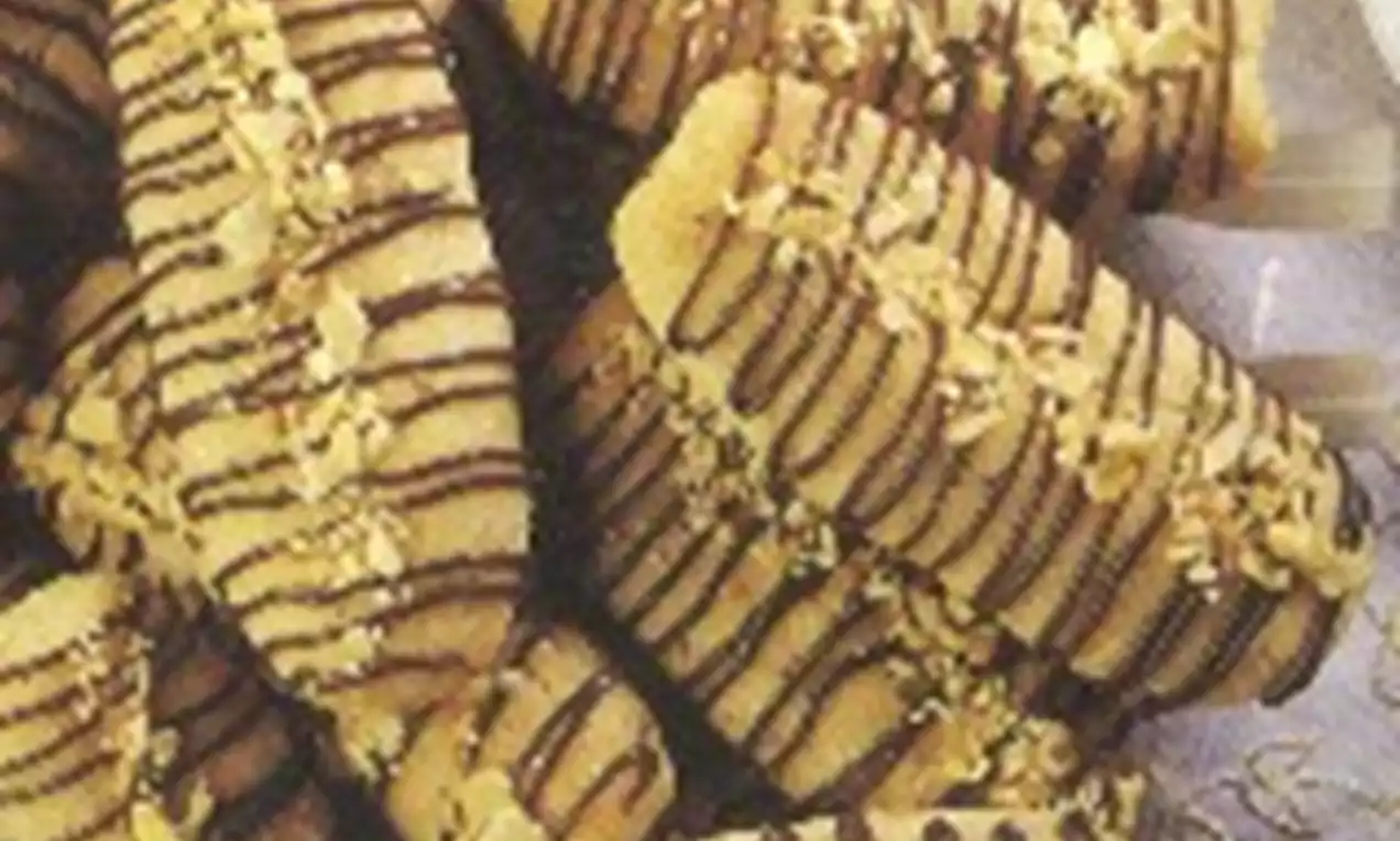 Bâtonnets dorés nervurés de chocolat foncé, parsemés de morceaux de noisettes sur une assiette transparente élégamment présentée