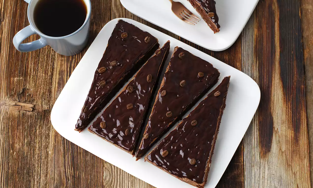 Koyu renkli ahşap zeminde beyaz tabakta yer alan çikolatalı kahveli ince dilim kekler parlak yüzeyli ve kahve çekirdekleriyle süslenmiş