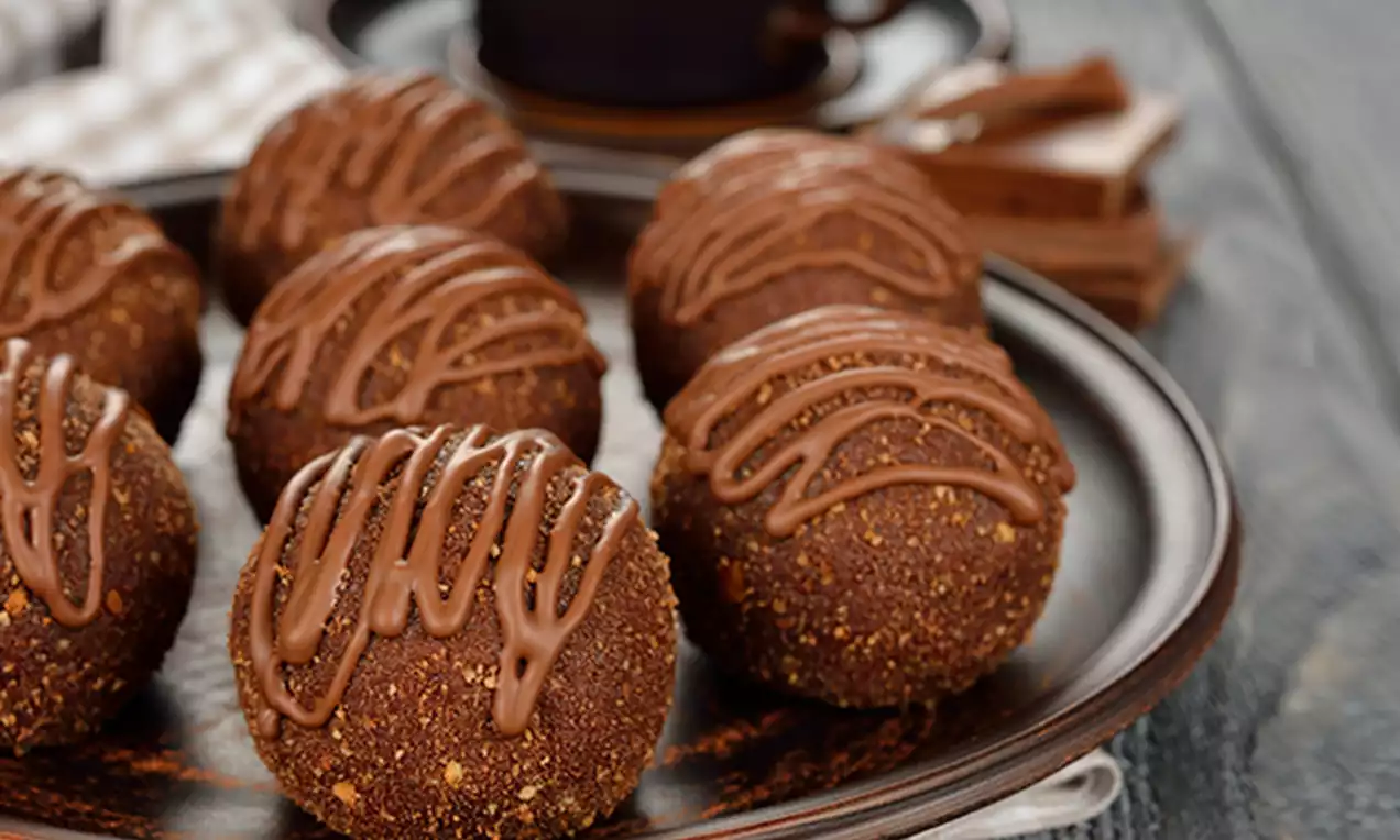 Round chocolate sponge cake pops covered in fine crumb coating and drizzled with milk chocolate, arranged on a dark plate