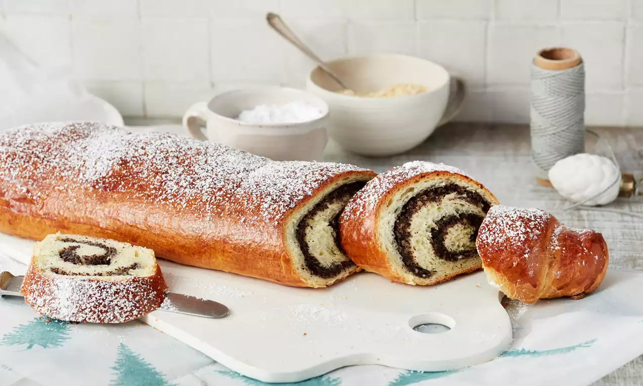 Goldbrauner Strudel mit zarter Mohnfüllung und Puderzucker bestäubt, angeschnitten auf Holzbrett mit winterlichem Tuch drapiert