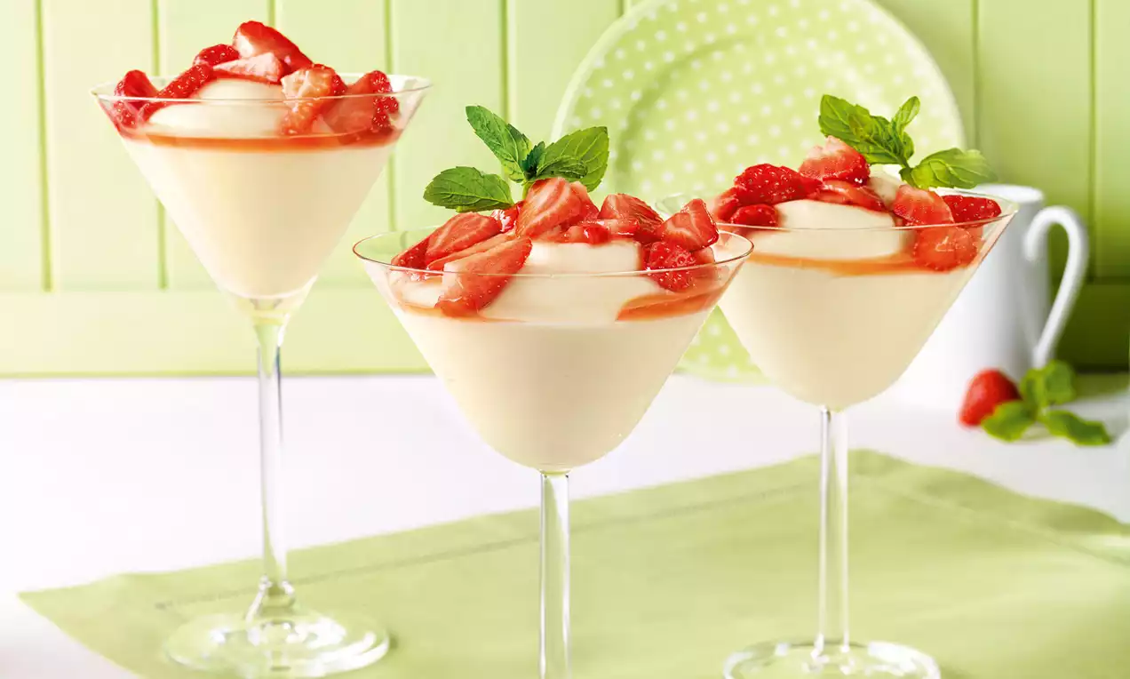 Cremiger Holunderblüten-Pudding in eleganten Cocktailgläsern, belegt mit glänzenden roten Erdbeerstückchen und frischen Minzblättern