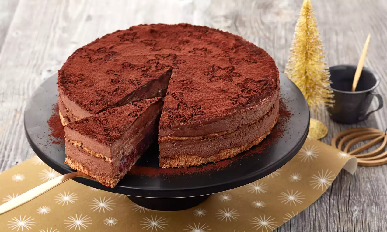 Schokoladenmousse-Torte mit brauner Kakaoschicht, cremigen Schichten und Keksboden, serviert auf schwarzer Tortenplatte mit goldener Weihnachtsdeko