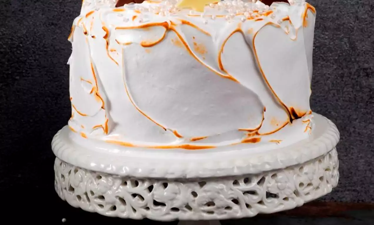 Kermaisen valkoinen marenkipäällyste, jossa oransseja pyörteitä, kakkua kruunaavat suklaasta ja valkosuklaasta tehdyt tähdet pitsilautasella