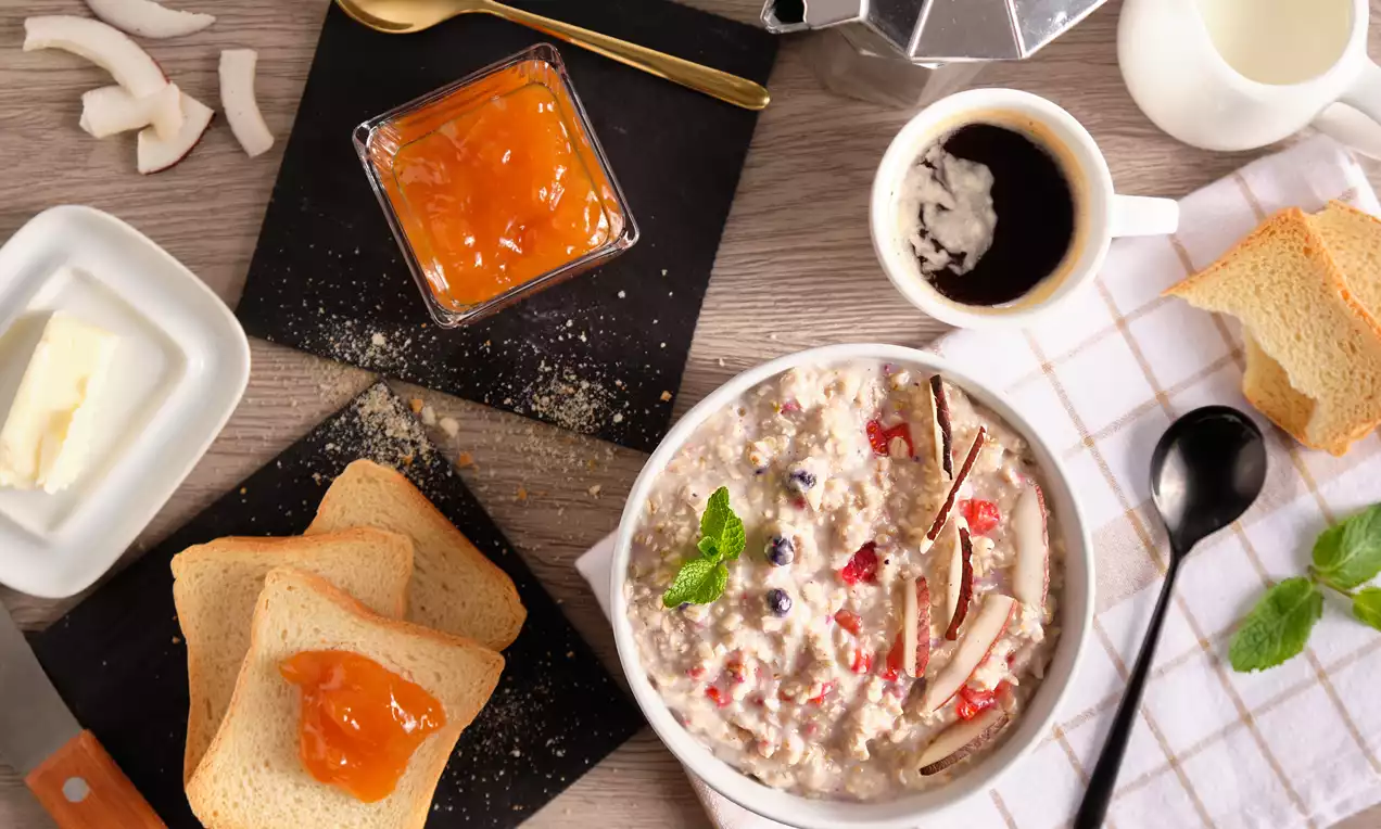Porridge cremoso dai toni chiari con frutti rossi e scaglie di cocco, guarnito con foglie di menta su un tavolo ricco di dettagli