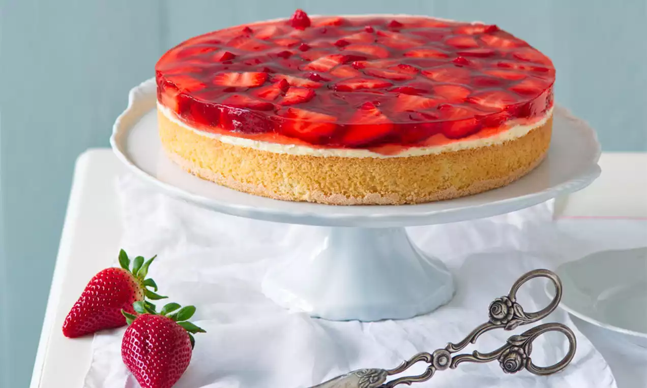 Jednoduchý jahodový tort s jemnou svetložltou piškótou, krémovou vrstvou a lesklým červeným želé s kúskami jahôd na bielom podnose