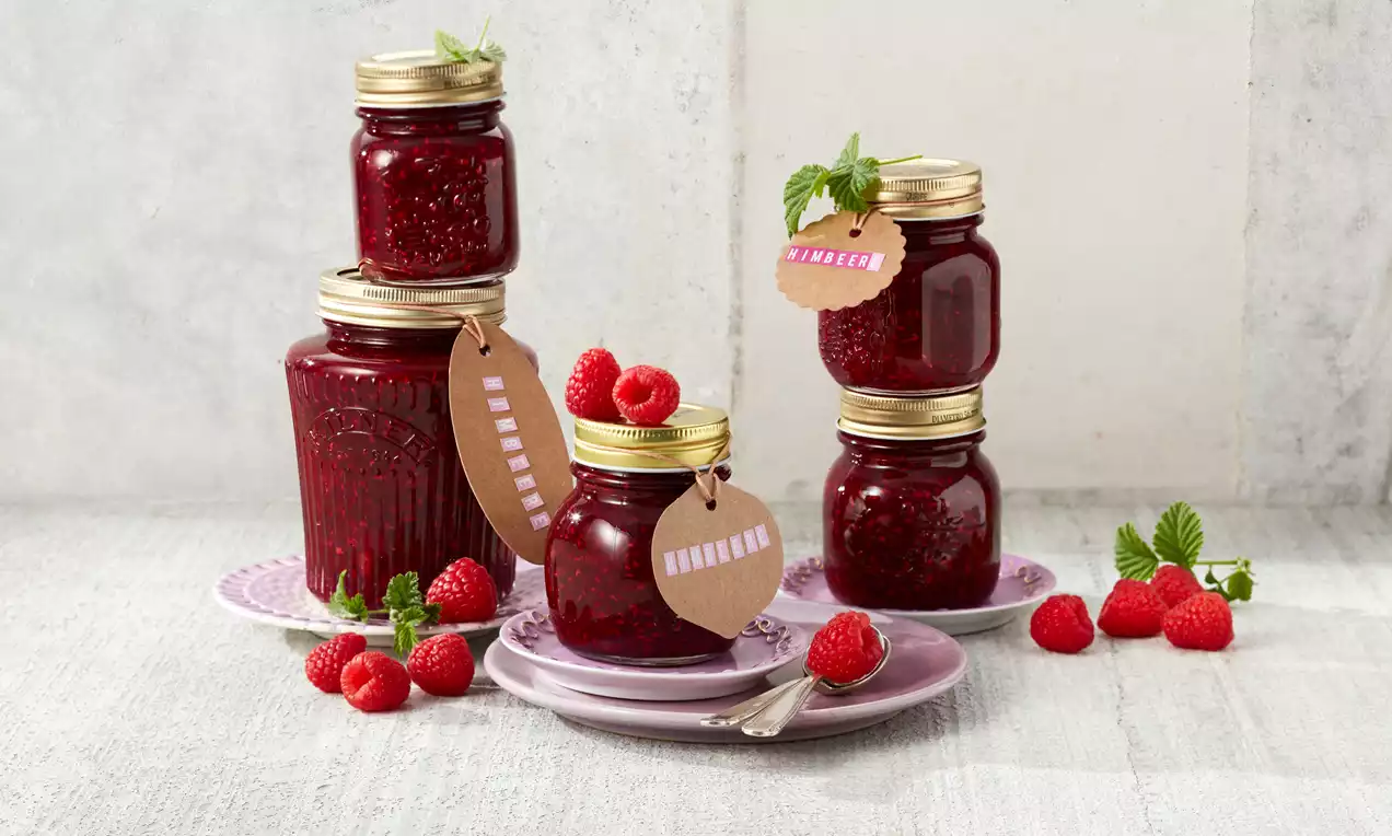 Himbeermarmelade in gläsernen Twist-Off-Gläsern, tiefrote Farbe, cremige Textur, dekoriert mit frischen Himbeeren und Minzblättern