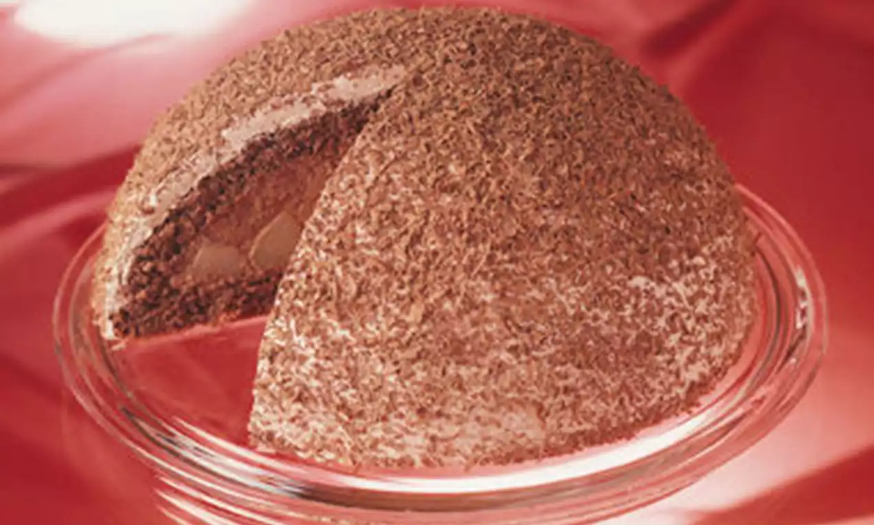 Halbrunde Kuppeltorte mit dunkler Schokoladenglasur und sichtbarer Füllung, serviert auf einem transparenten Glasteller vor rotem Stoff