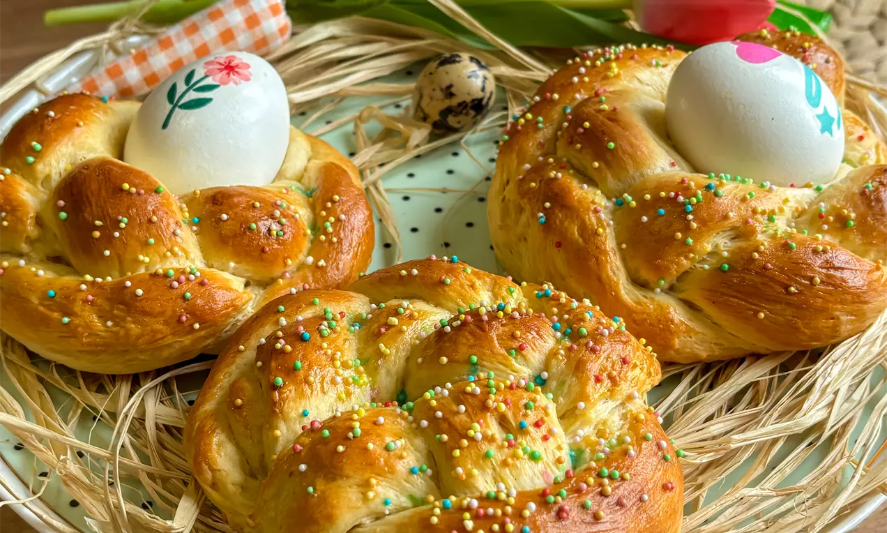 Pleteni slatki kruščići zlatnosmeđe boje posuti šarenim mrvicama, svaki s jajetom u središtu, na podlozi od slame i tanjura