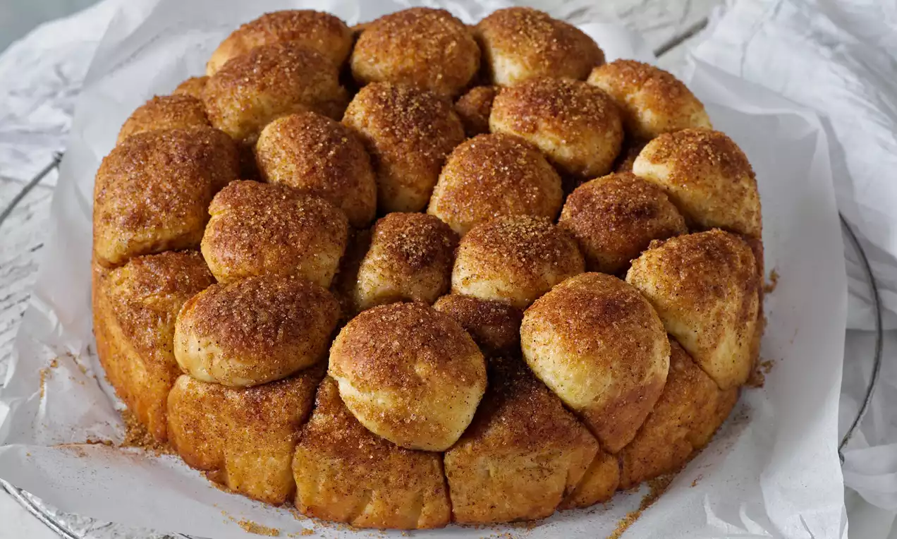 Nadýchané koule dozlatova upečeného těsta posypané skořicovým cukrem, seskládané do kruhového tvaru na bílém pečicím papíru