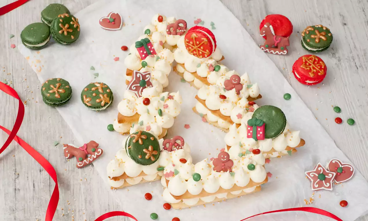 Weihnachtlicher Tannenbaum-Cookie-Cake mit weißer Creme, bunten Streuseln, grünen und roten Macarons sowie Lebkuchenfiguren verziert