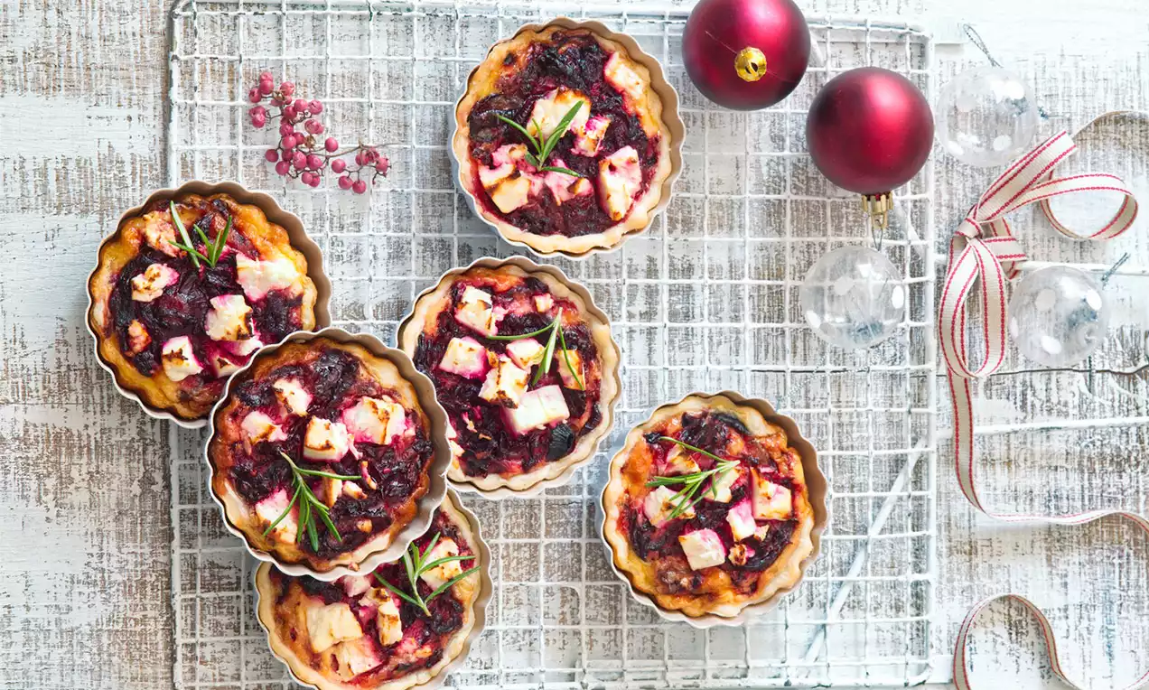 Malé okrúhle tartaletky so zlatistým okrajom, plnené červenou repou, kúskami bielej fety a ozdobené vetvičkami rozmarínu na mreži