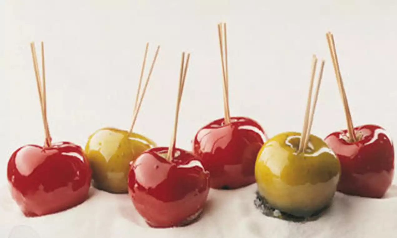 Rot- und gelbglänzende Paradiesäpfel mit glatter Zuckerkruste, auf Holzstäben gesteckt und nebeneinander auf hellweißem Untergrund arrangiert
