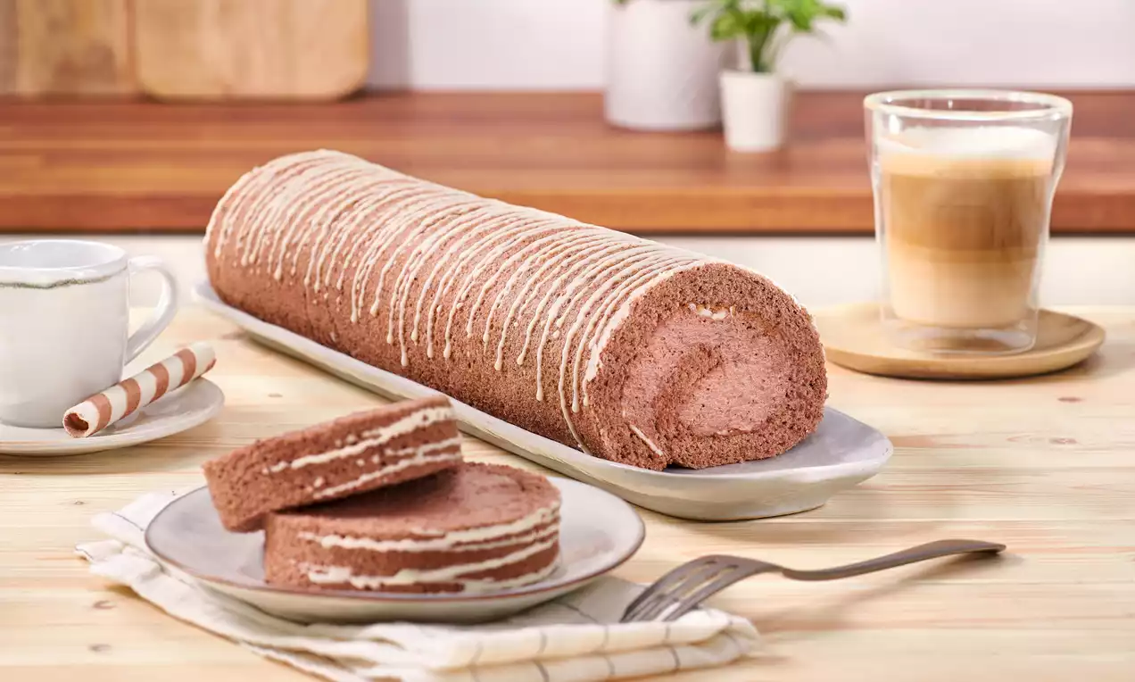 Lockere, braune Schoko-Sahne-Rolle mit heller Cremefüllung und weißen Streifen auf heller Platte, serviert mit Kaffee und Besteck