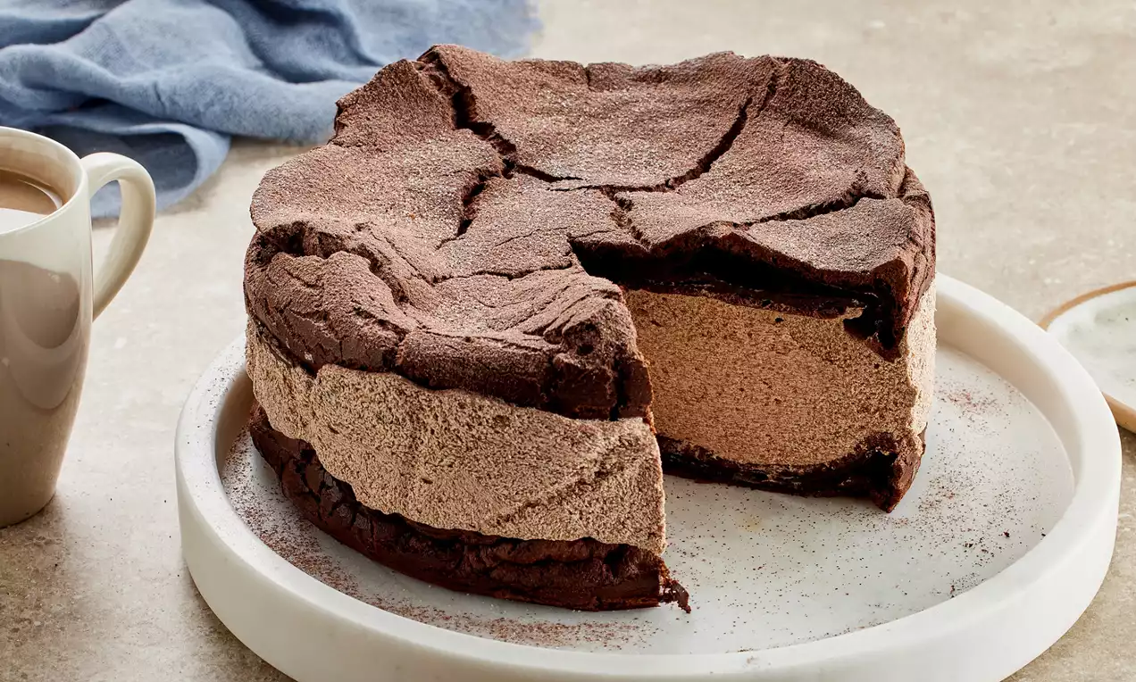 Kakao renkli çatlamış üst tabakası, kremalı kahverengi dolgusu ve yumuşak katlarıyla beyaz tabakta sunulmuş çikolatalı Karpatka