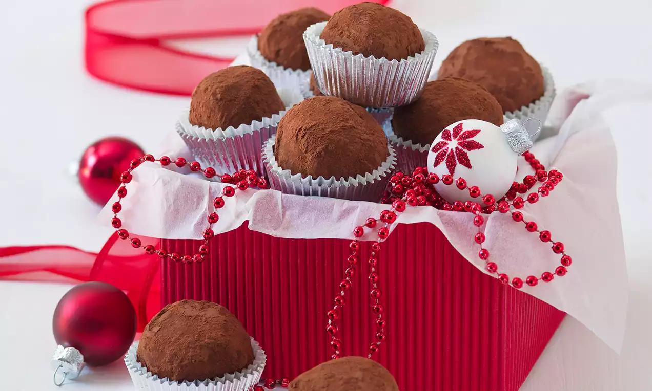 Marcipánové guľky v jemnom kakaovom poprášení, uložené v strieborných košíčkoch v červenej darčekovej škatuli zdobenej stuhou a vianočnými dekoráciami