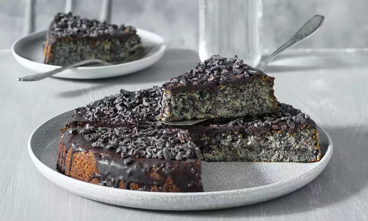 Bezlepkový makový dort s bohatou čokoládovou polevou a strúhanými čokoládovými kúskami na svetlosivom keramickom tanieri