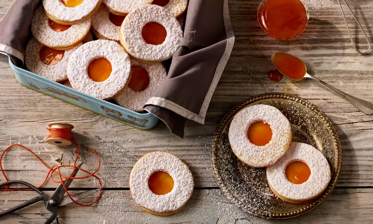 Linzer Kekse mit Puderzucker bestäubt, runde Form und orangene Marmeladenfüllung, auf einem goldenen Teller und in einer Dose angerichtet