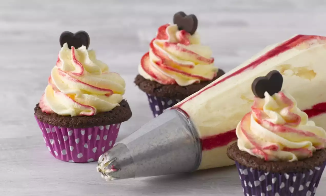 Pienet suklaamuffinit purppuraisissa pilkkukapseleissa, päällä kermavaahdosta tehty vaaleankeltainen ja vadelmanpunainen spiraalikuorrute sekä suklaasydän