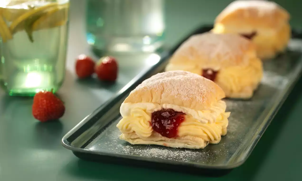 Žltkastý krém jemne vytlačený medzi nadýchané oblúkové vrstvy cesta, s červeným jahodovým džemom uprostred, posypané práškovým cukrom