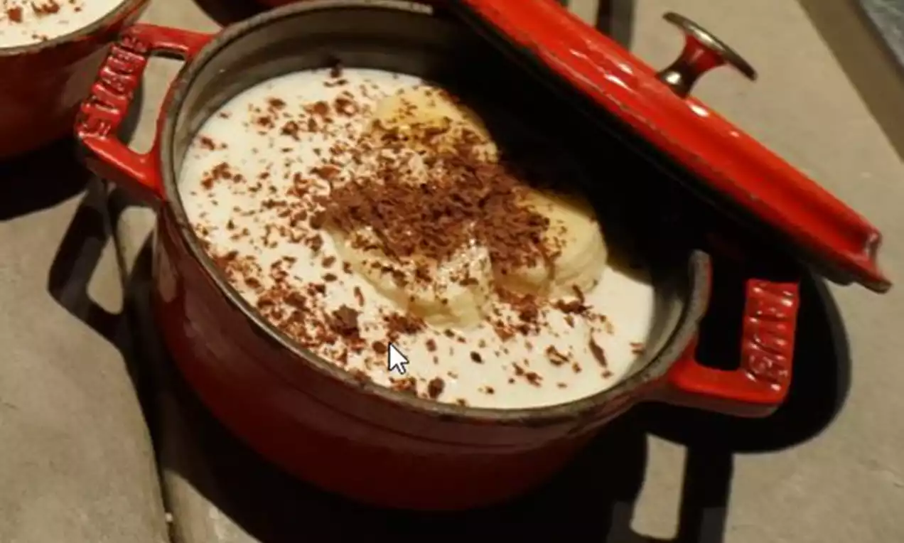 Romige cheesecakevulling met plakjes banaan en geraspte chocolade, geserveerd in een rode, open cocotte op een stenen ondergrond