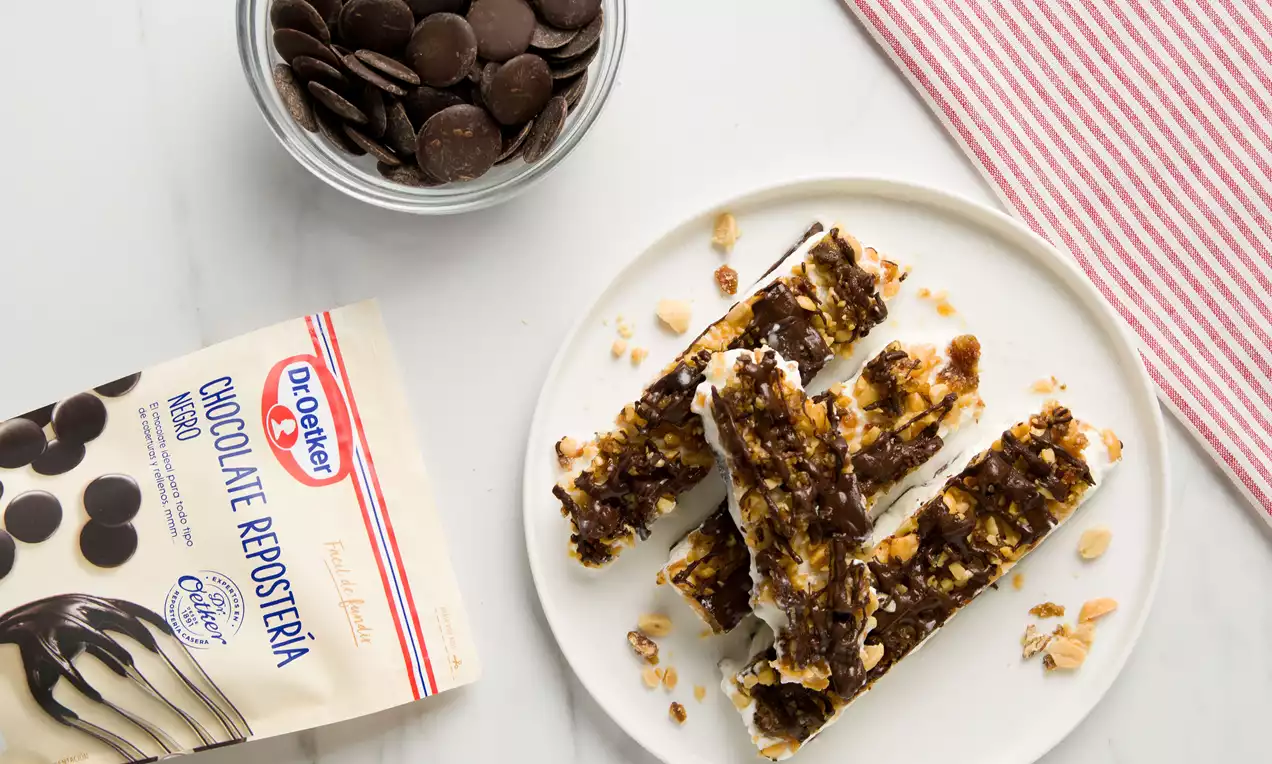 Barritas alargadas con base blanca y superficie irregular de chocolate oscuro y trozos de cacahuetes servidas en un plato blanco