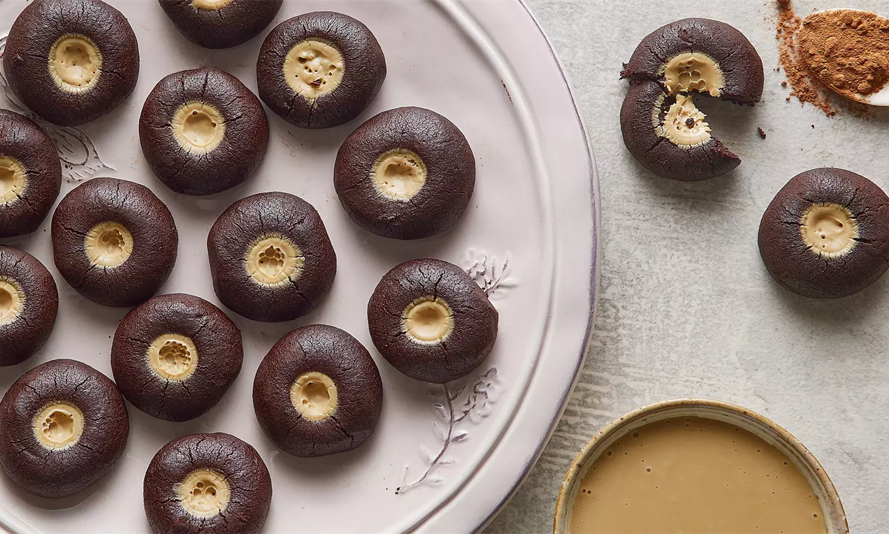 Kakaolu dış yüzeyi pürüzsüz, hafif çatlak dokulu, ortası açık renkte tahin dolgulu yuvarlak kurabiyeler pastel renkli bir tabakta sunulmuş