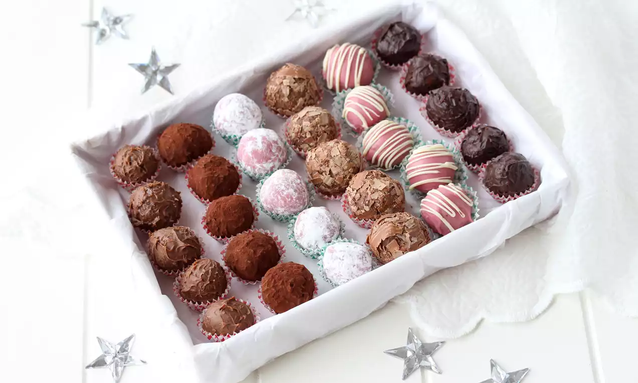 Trøffelkuler med ruby-, lys og mørk sjokolade i ulike teksturer og dekor, plassert tett i hvit eske med stjerner på hvitt underlag