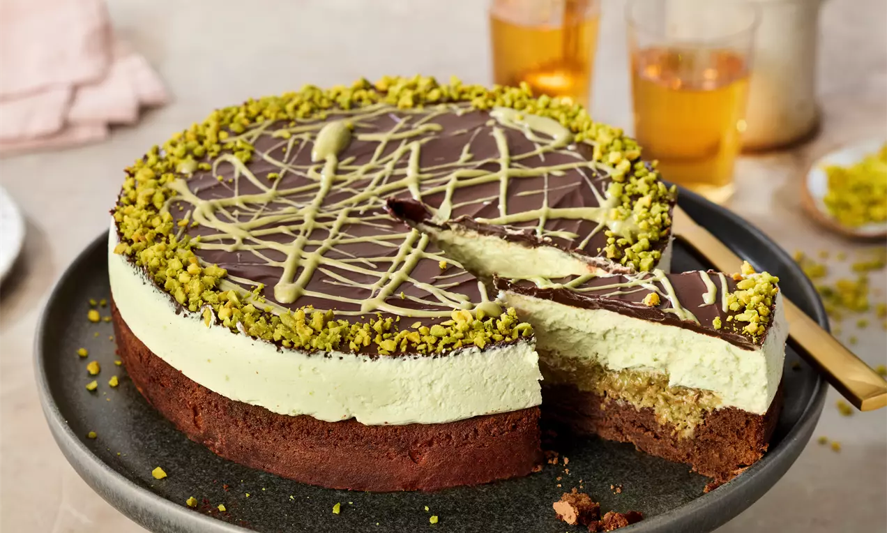 Dubai torte with layers of chocolate glaze, green pistachio cream and golden sponge, topped with pistachio crumbs on a dark plate