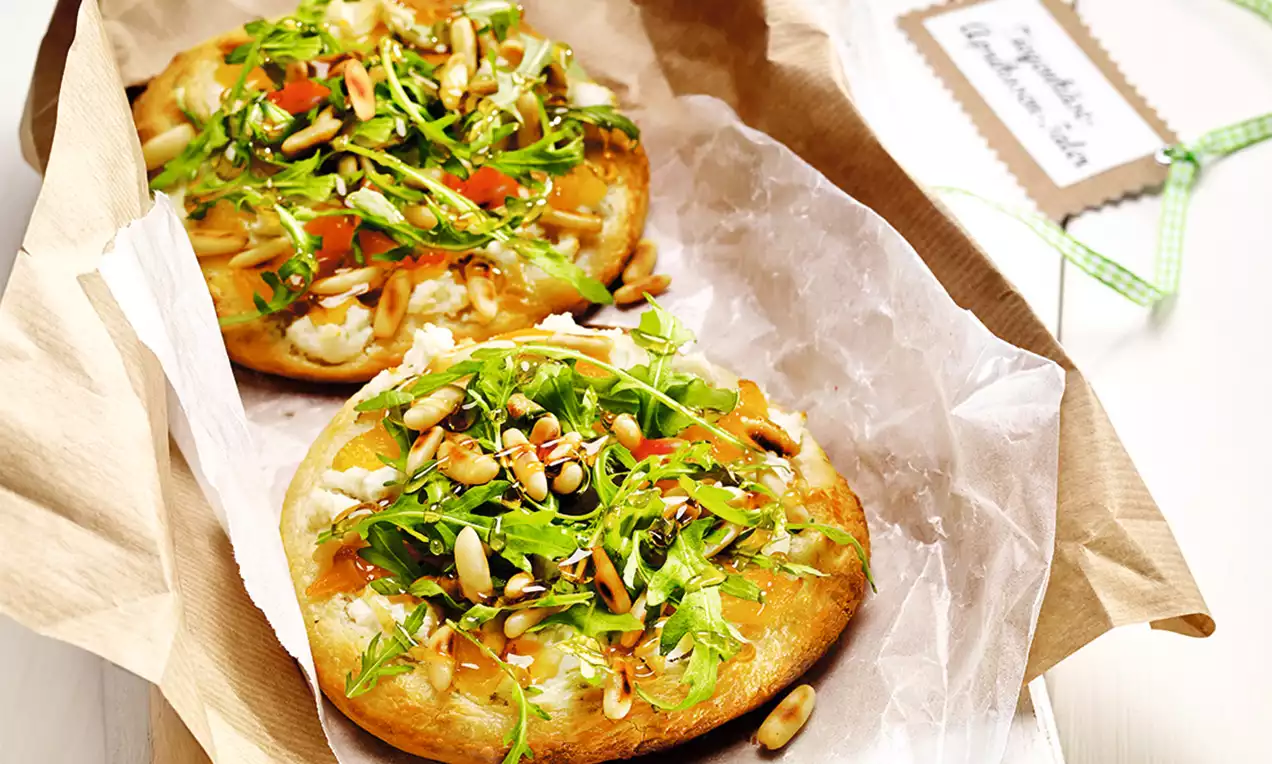 Slané meruňkové koláče s měkkou zlatavou kůrkou, pokryté rukolou, piniovými semínky, kousky meruněk a drobeným sýrem na pečicím papíře