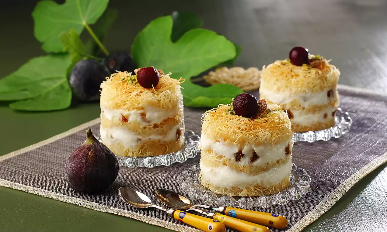 Cam tabaklarda servis edilen tel kadayıflı tatlı, kremamsı dolgu, ince kadayıf kıtırları ve kırmızı kirazlarla süslenmiş