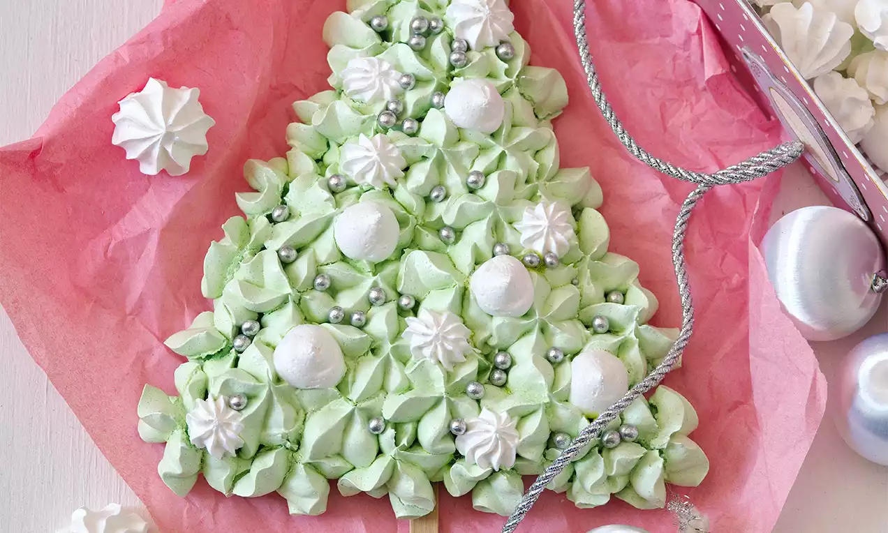 Světlý zelený stromeček z křehkých pusinek, s bílými cukrovými ozdobami a stříbrnými kuličkami, položený na růžovém papíře