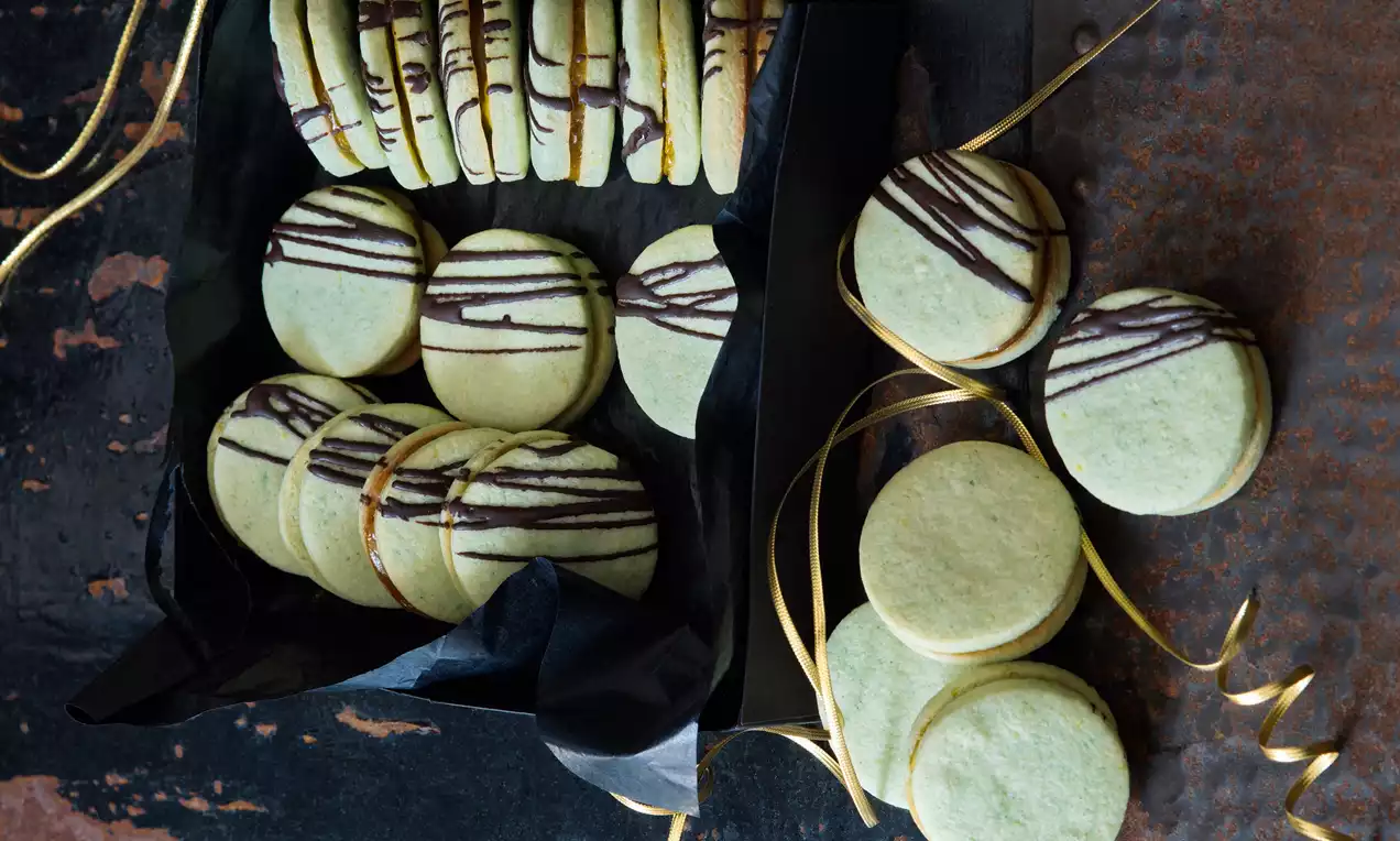 Svetlozelené guľaté kolečka s jemným čokoládovým pásikovaním, usporiadané v čiernom papierovom obale a na tmavej podložke so zlatou stuhou