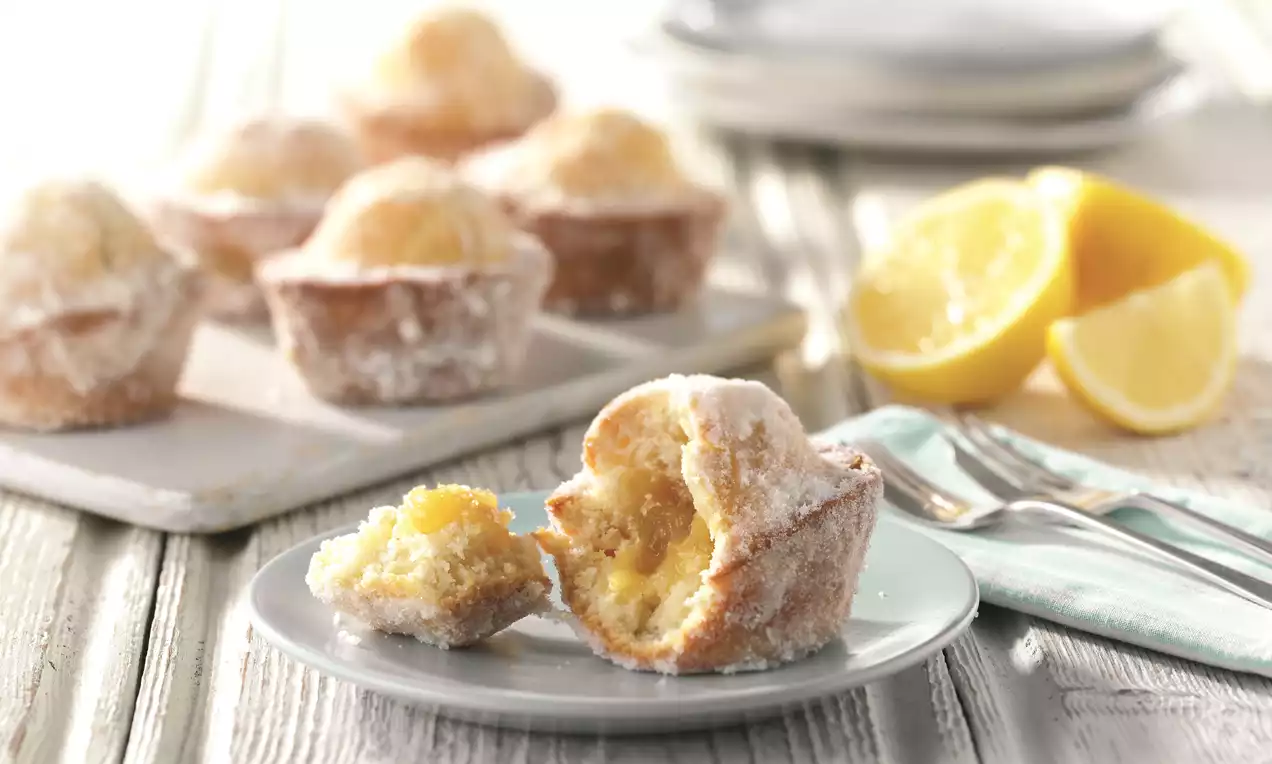 Lemon duffins dusted with sugar, golden and round with soft crumbly texture, one split open on a plate near halved lemons and cutlery