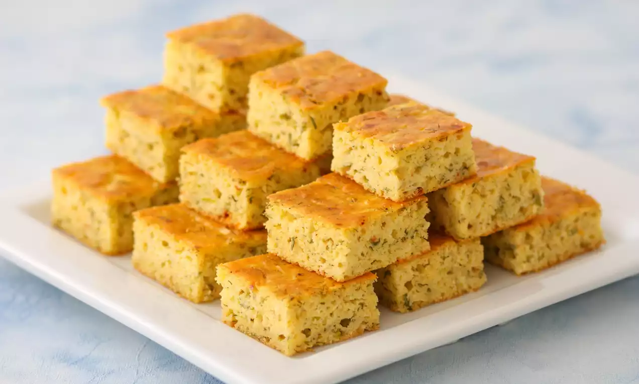 Küp şeklinde kesilmiş altın sarısı kabaklı tuzlu kek dilimleri, beyaz kare tabakta simetrik olarak üst üste dizilmiş şekilde sunulmuş