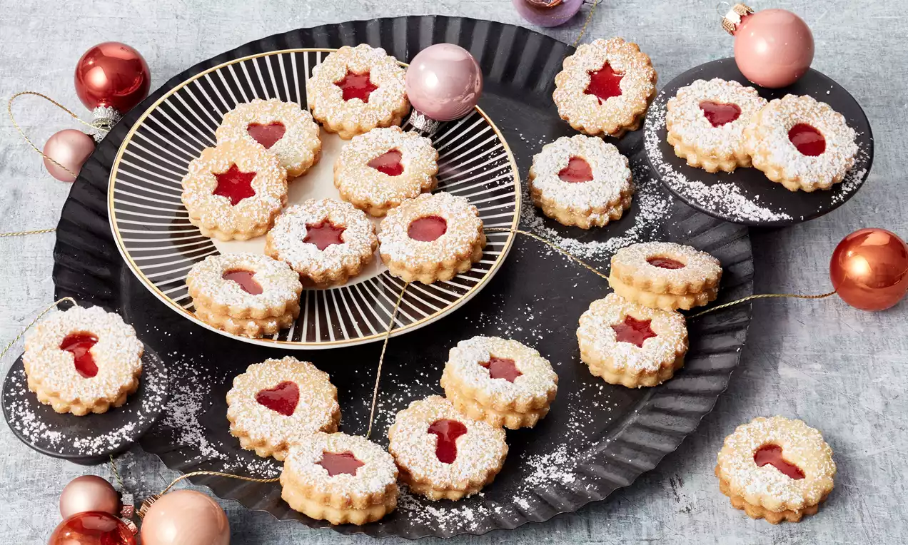 Spitzbuben mit roter Himbeermarmelade, goldbraunen Teigrändern und sternförmigen Ausstanzungen, auf einem rustikalen Holzbrett angerichtet