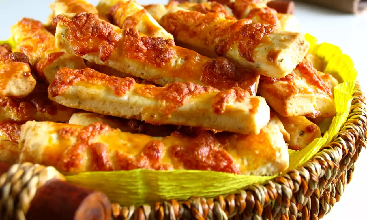 Kızarmış altın rengi kaşarlı dilimler, örgü bir sepette sarı kağıt üzerinde düzenli şekilde yerleştirilmiş