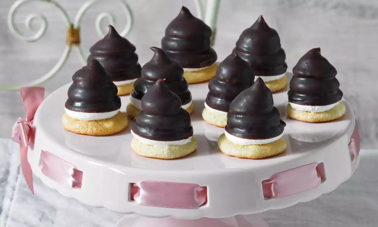 Indiáni s lesklou tmavou čokoládovou polevou na vrstve bieleho krému, uložené na svetlých piškótach na svetloružovom podnose s mašľami