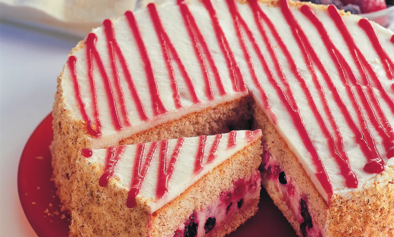 Grieß-Beerentorte mit heller Creme und roten Fruchtstreifen, geschnitten auf rotem Teller, gefüllt mit Beeren und mit Bröseln bestreut