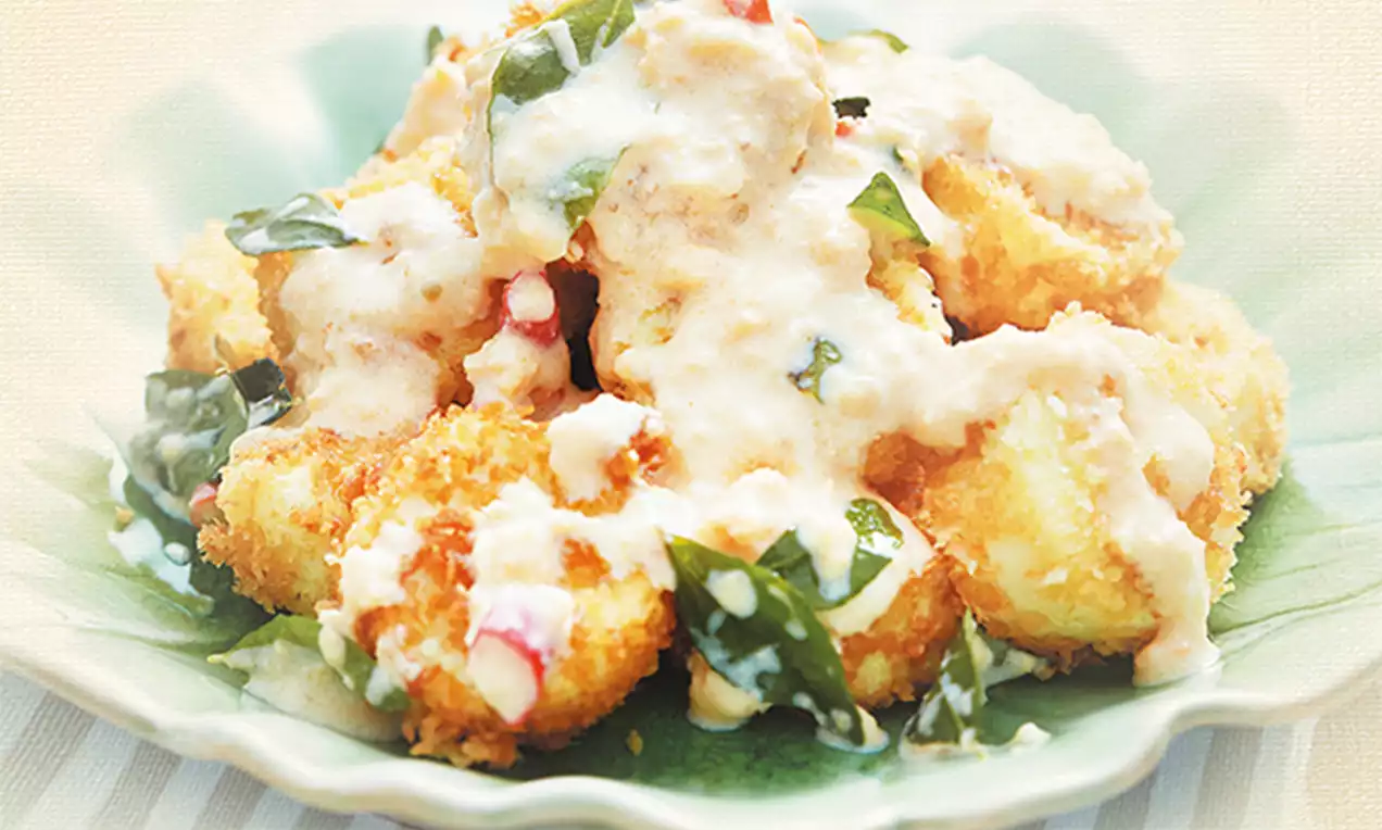 Golden cubes of tofu coated in crisp breadcrumbs, drizzled with creamy salted egg sauce, topped with green curry leaves on a green plate