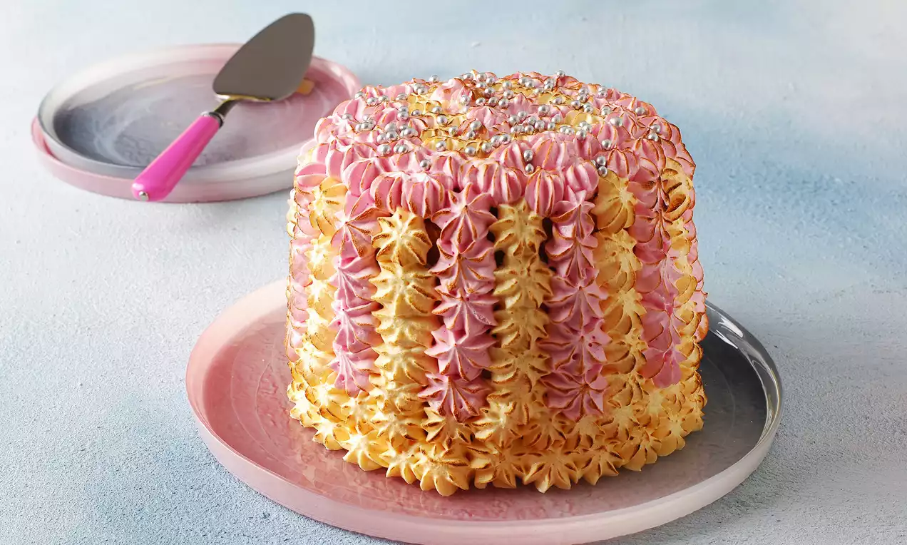 Pembe ve sarı merenglerle kaplanmış, desenli yıldız uçlu krema dokusu bulunan, inci şekerlerle süslenmiş yuvarlak pasta pembe bir tabakta