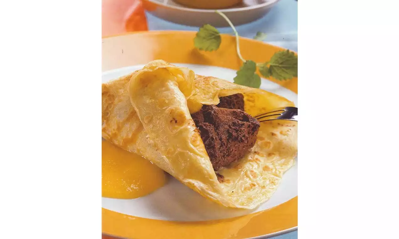 Crêpe dorée pliée et garnie de mousse au chocolat brun, posée sur une assiette avec une sauce jaune brillante et une feuille verte