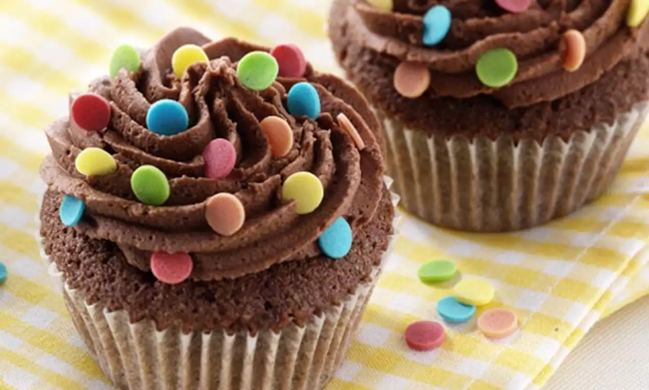Cupcakes au chocolat moelleux surmontés d'une spirale de crème chocolatée et parsemés de confettis colorés, posés sur un tissu rayé jaune