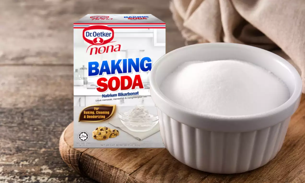 A white ribbed ramekin filled with fine white baking soda on a rustic wooden surface with a beige cloth and a box of baking soda