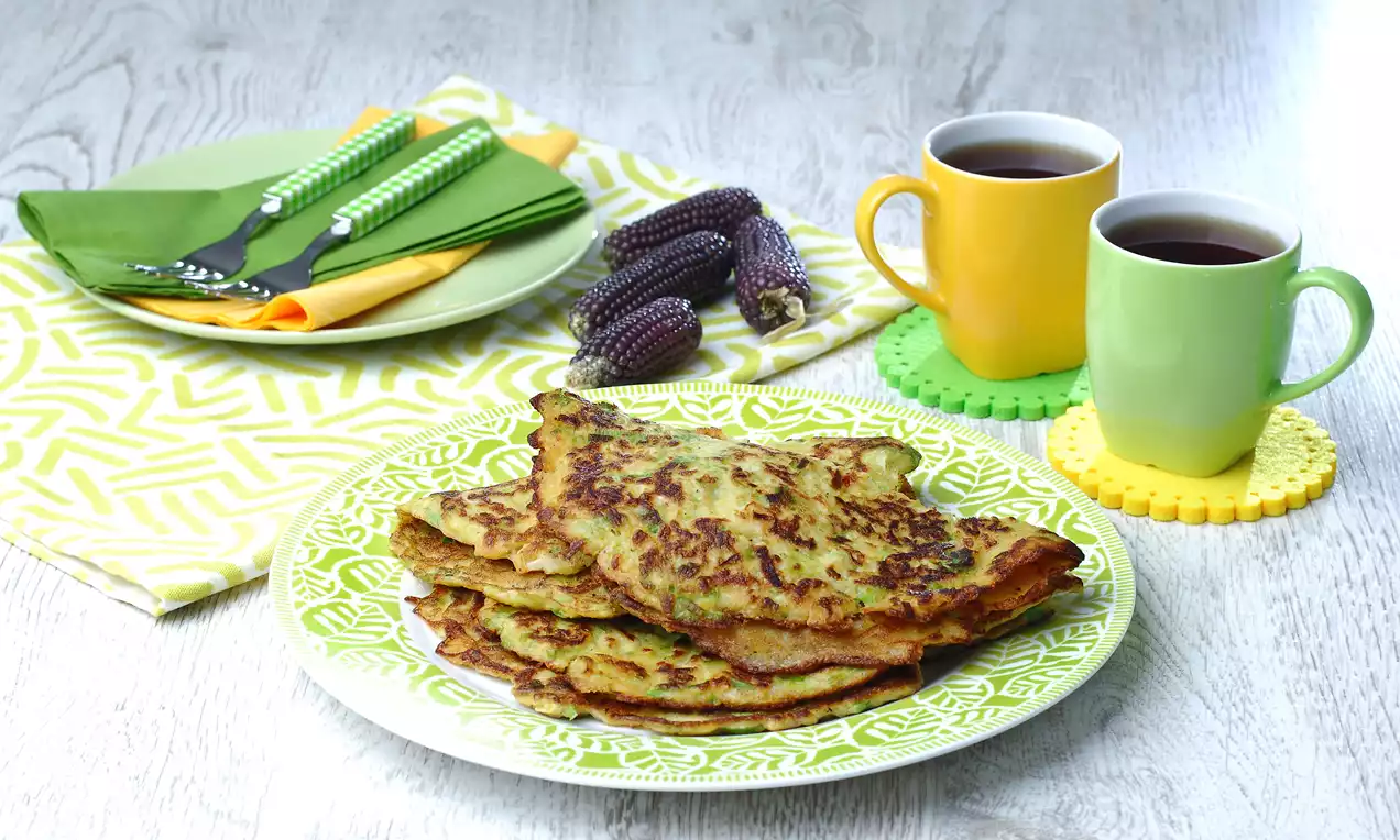 Yeşil desenli tabakta altın rengi ve hafif yanık yüzeye sahip pırasa tava, yanında iki renkli kupa ve dekoratif mor mısırlar ile sunulmuş