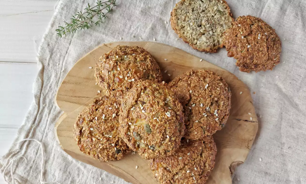 Zlatohnedé semienkové bochánky s chrumkavým povrchom, posypané ovsenými vločkami, sú usporiadané na drevenej doske vedľa vetvičky rozmarínu