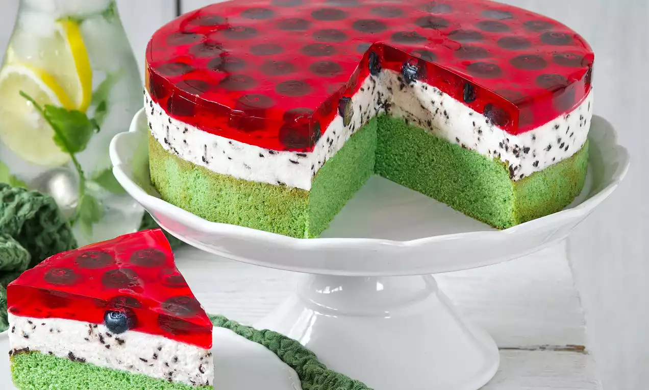 Letní Krtkův dort s jasně zeleným piškotem, vrstvou světlého krému s čokoládovými kousky a průhlednou červenou želatinou s borůvkami na podnosu