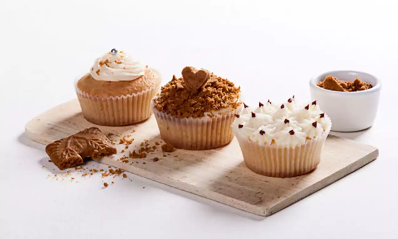 Drie cupcakes op een houten plank, versierd met slagroom, speculooskruimels, een speculooshartje en chocoladedruppels, met een schaaltje speculooscrème ernaast