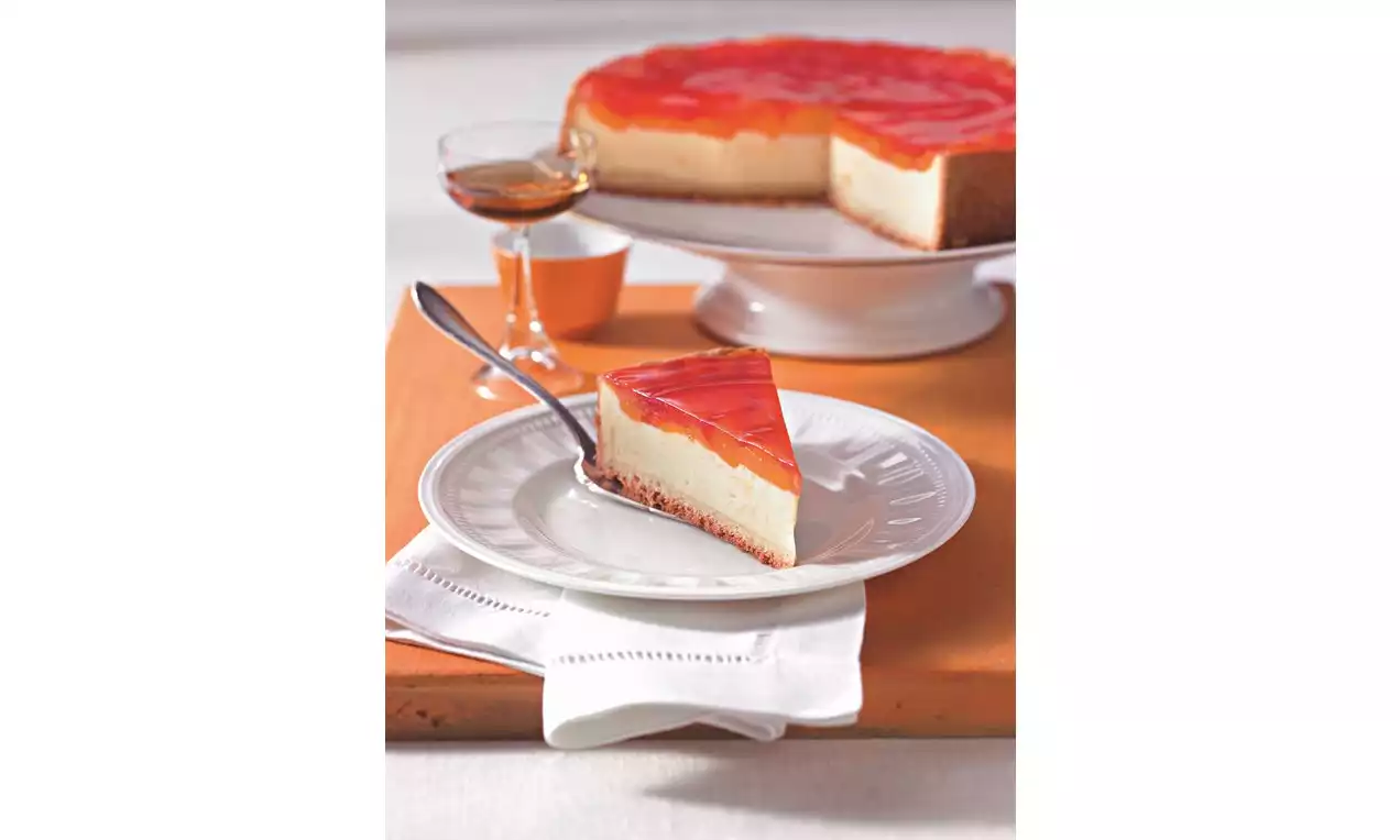 Kremasti kolač od sira na svijetlosmeđoj podlozi, prekriven prozirnim slojem želea s komadićima mandarina, na bijelom tanjuru