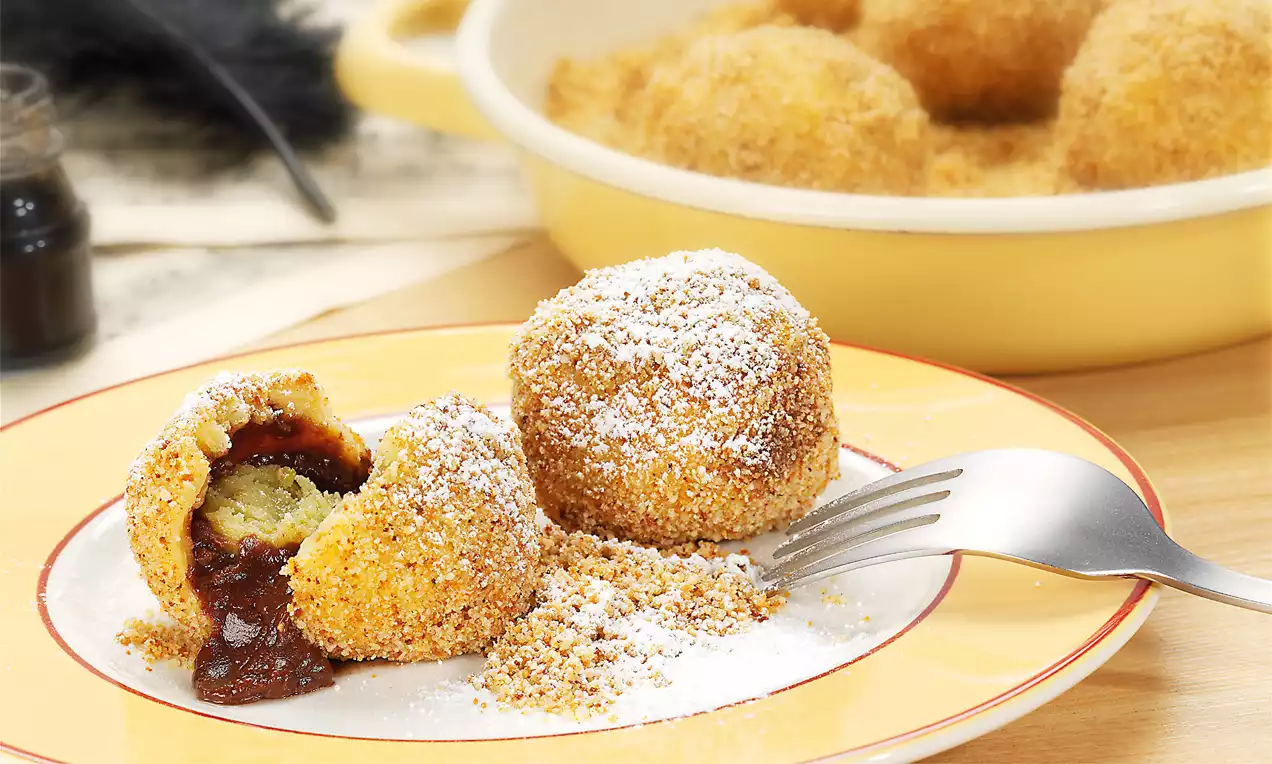 Goldbraune Mozartknödel mit knuspriger Bröselhülle, zartem Nougatkern und Staubzucker bestäubt auf einem Teller mit Gabel angerichtet